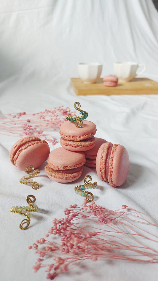 Four handmade wire wrapped rings on top of pink macarons